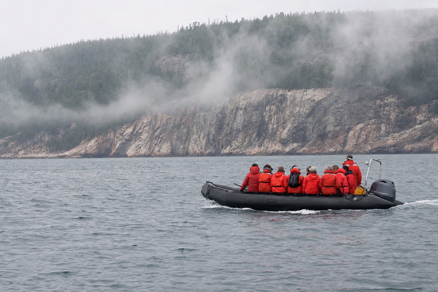 Zodiac of whale watchers in red flotation suits on the St. Lawrence estuary near Tadoussac, fog lifting off the far shore