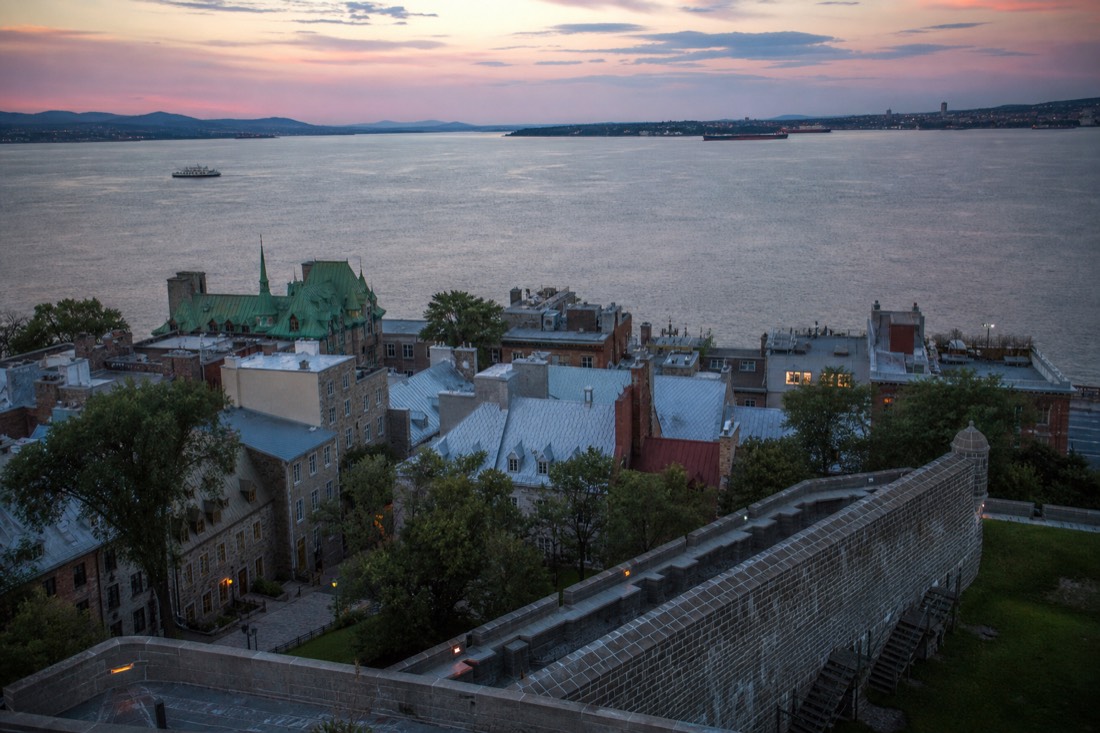 Old Quebec rooftops and fortification walls at dusk with the St. Lawrence River beyond
