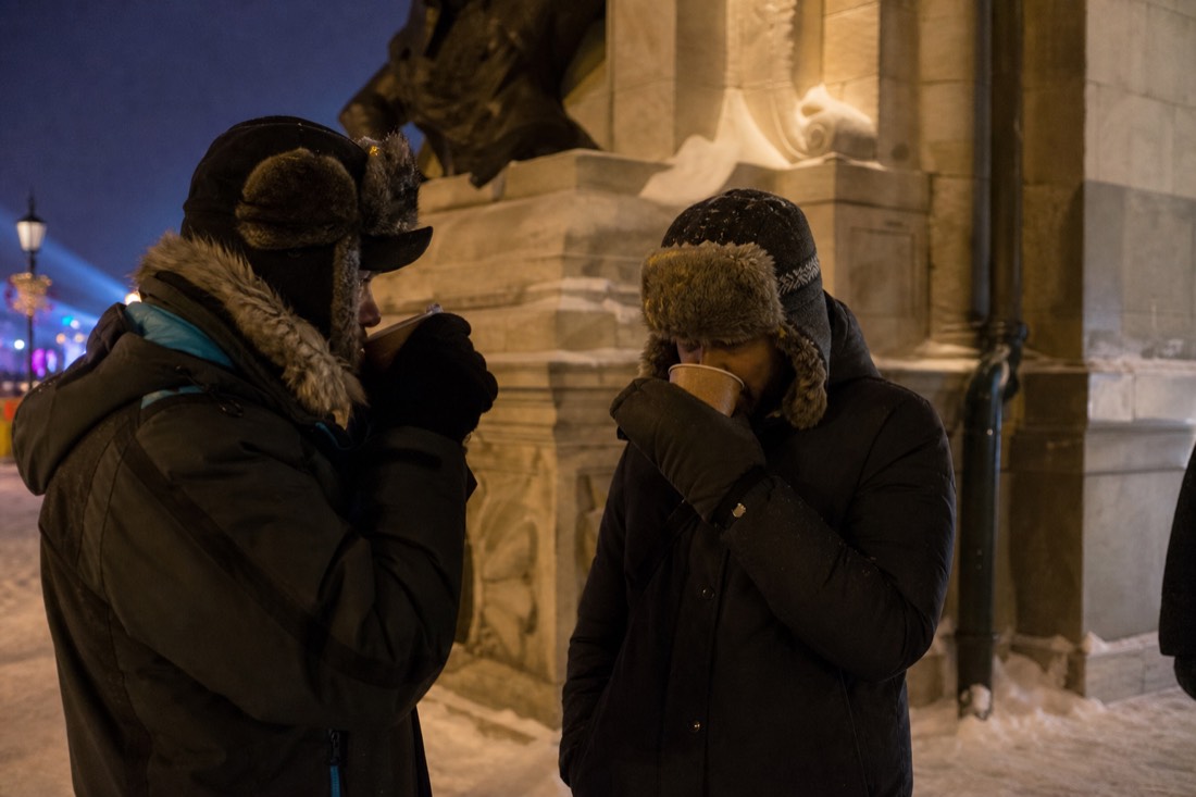 Visitors in heavy parkas mitts and fur hats warming up with hot drinks at the Quebec Winter Carnival at night