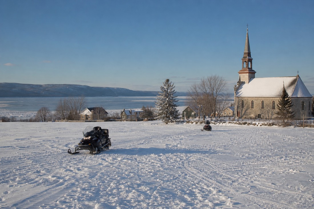 Snowmobiles crossing a snowy field on Île d'Orléans near Quebec City on a clear winter day