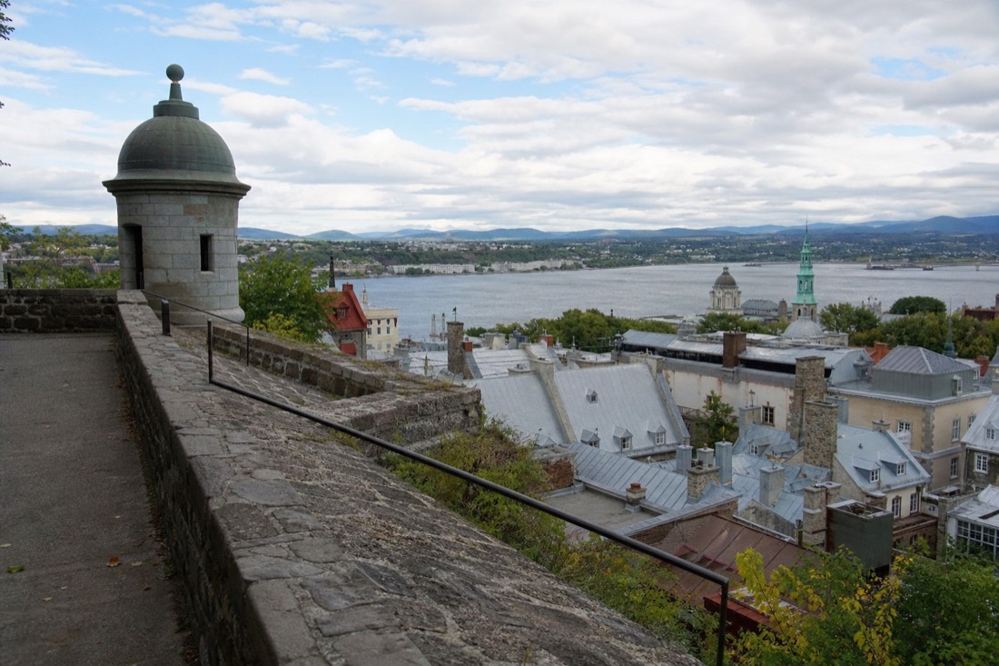 Visitors walking the stone ramparts of Old Quebec with rooftops and the river beyond