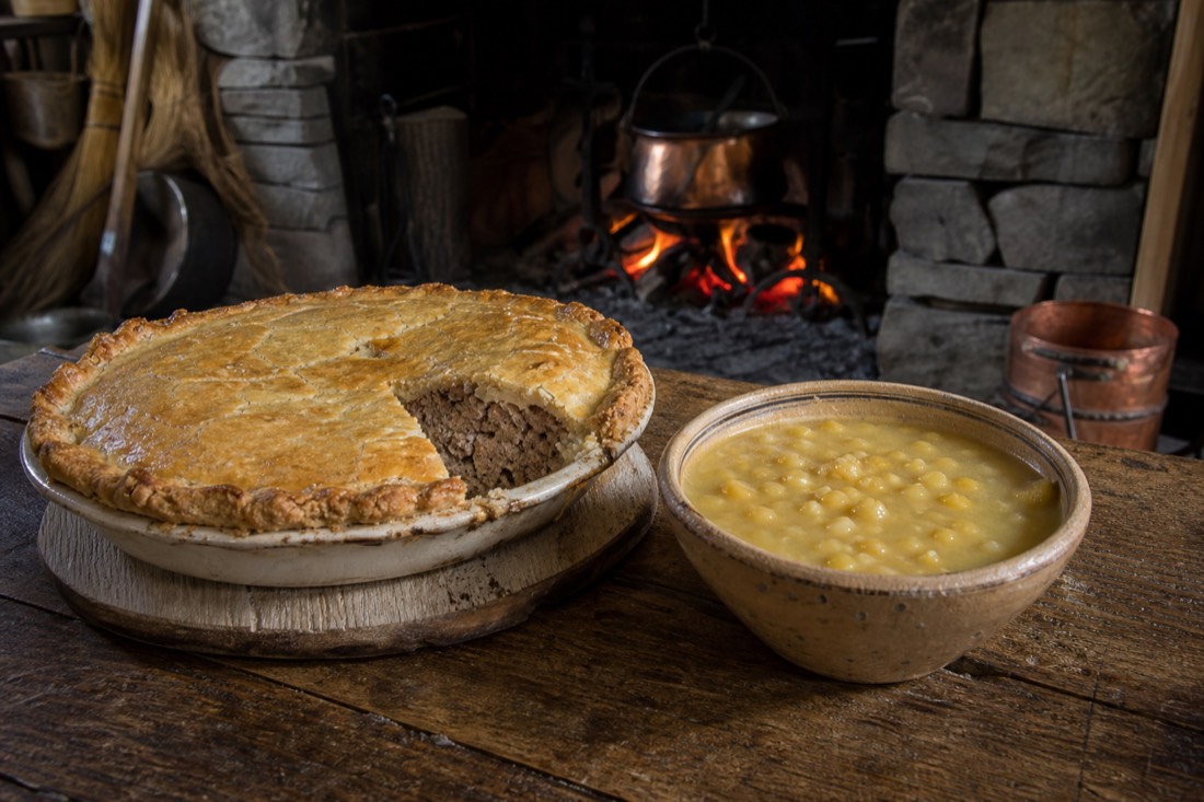 Golden-crusted tourtière meat pie beside a bowl of yellow pea soup on a rustic Quebec table