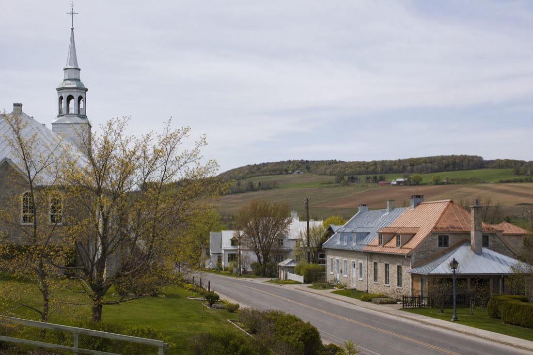 Stone church and old houses along the main road of a village on Île d'Orléans with farm fields behind
