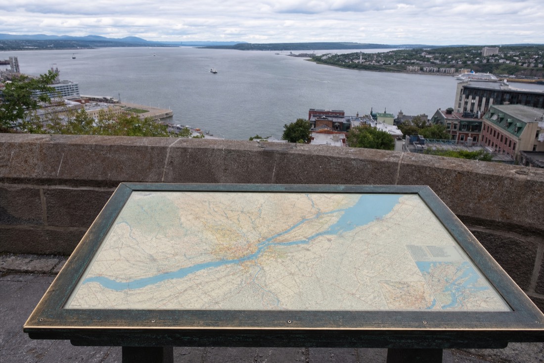 Traveler comparing Montreal and Quebec City routes on a map beside the St. Lawrence River
