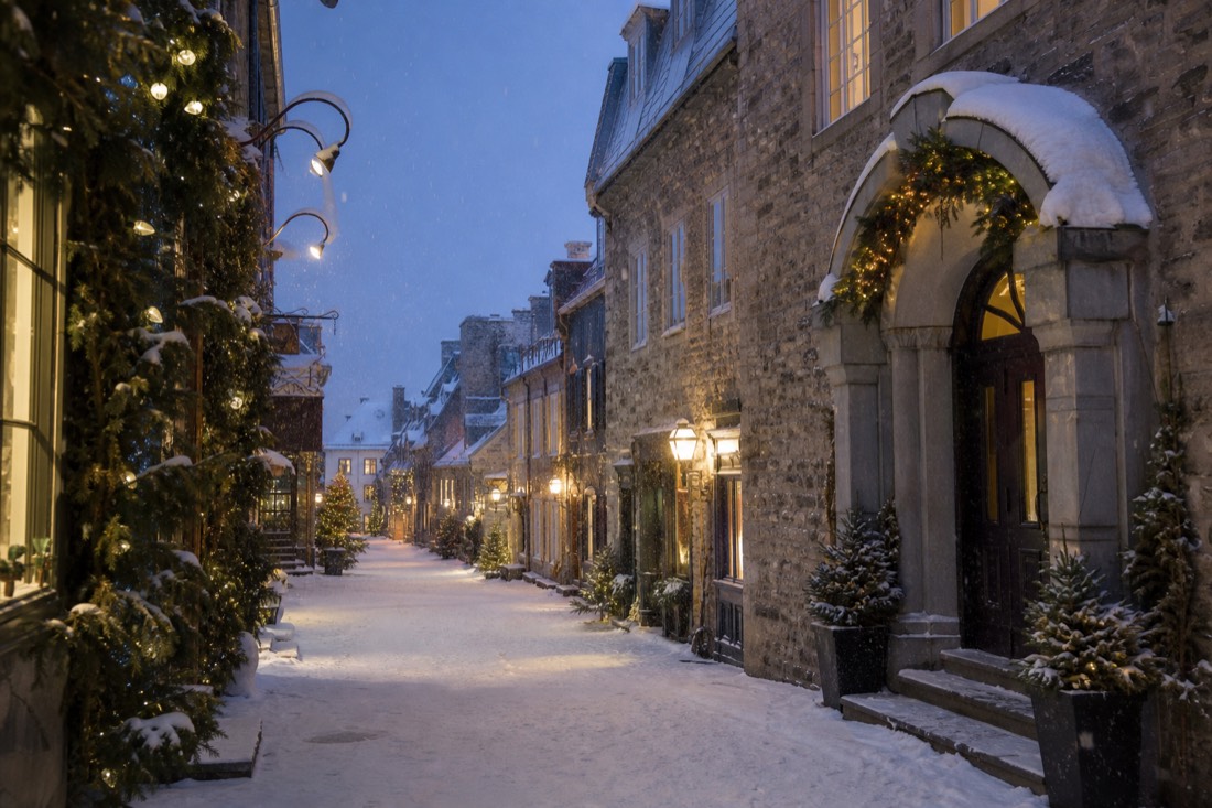 Shoppers on a snowy evening in the Petit Champlain district with lit storefronts and garlands